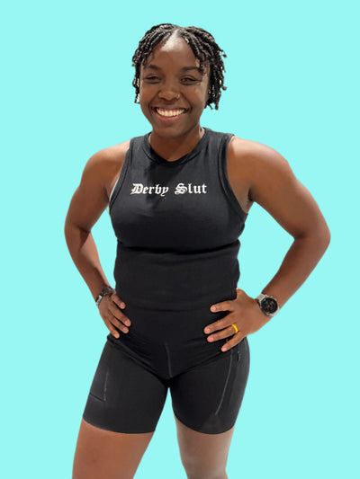 Woman wearing a black tank top with 'Derby Slut' text at an indoor event.